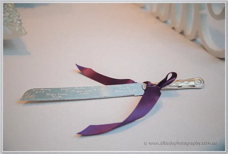 Engraved silver cake knife tied with plum ribbon resting on the white tablecloth