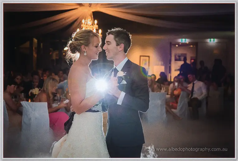 Lauren and Ryan gazing at each other mid first dance, lens flare sparkling between them in the dim ballroom