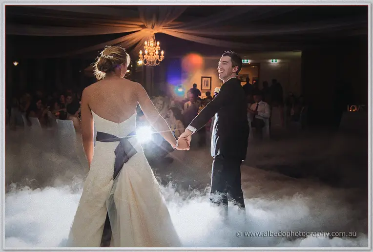 Ryan leading Lauren by one hand across the fog-dusted floor, her bow-backed gown lit from behind