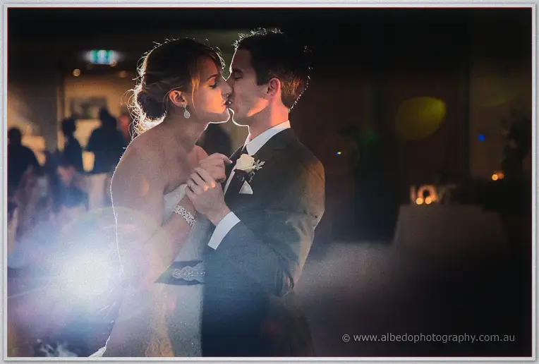 Lauren and Ryan kissing mid-dance, warm flare washing the dark reception room behind them