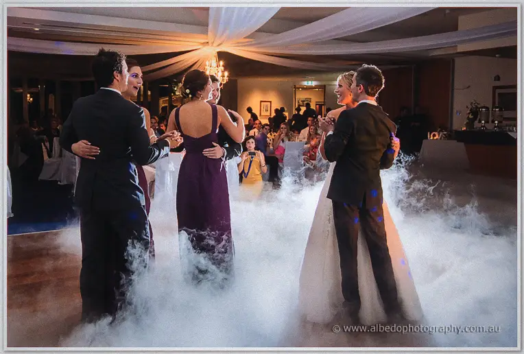 Two couples swaying in fog on the floor, bridesmaids in plum gowns dancing with their partners at the reception
