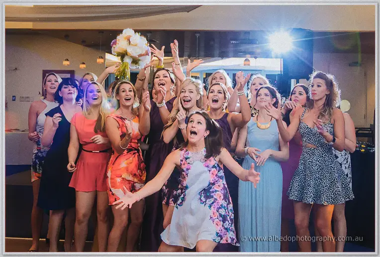 Excited women leaping with outstretched arms as the bouquet sails above them during the toss