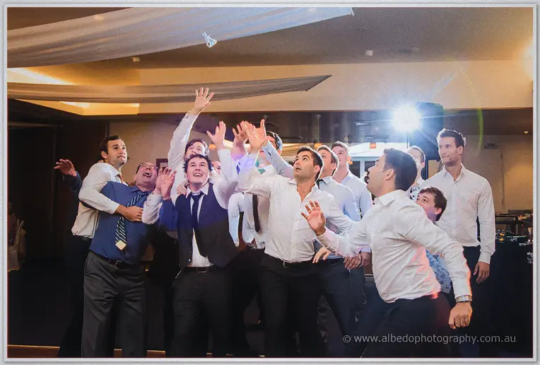 Pack of men leaping with arms stretched for the garter flying high above the dance floor