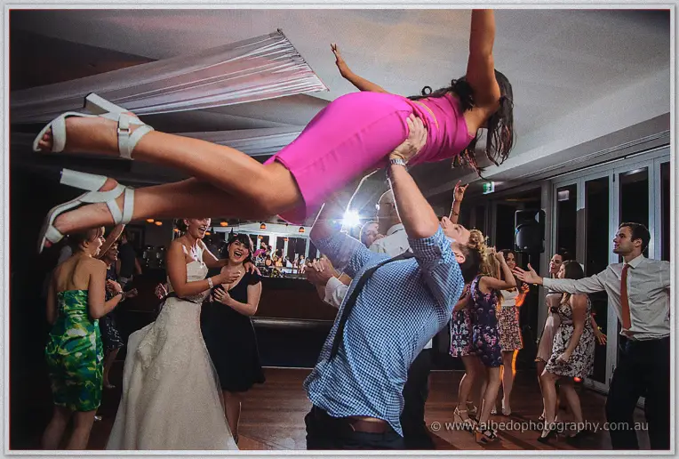 Dancer in checked shirt lifting his partner in pink high overhead mid-dance as the bride laughs nearby