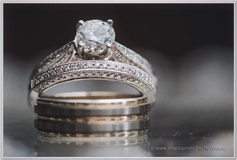 Macro of the solitaire engagement ring stacked on its pavé band beside Ryan's gold wedding rings