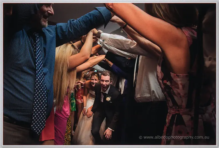 Lauren and Ryan ducking hand-in-hand through a tunnel of raised guests' arms as they exit the reception