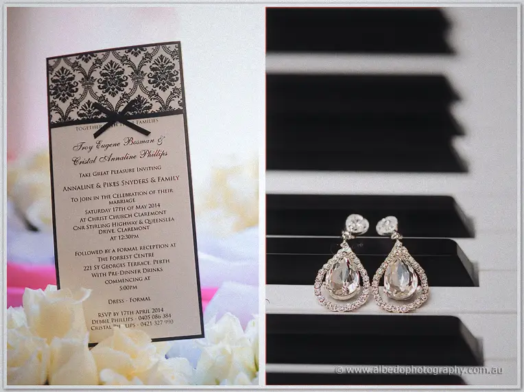 A damask wedding invitation tied with black ribbon sits beside crystal teardrop earrings on piano keys