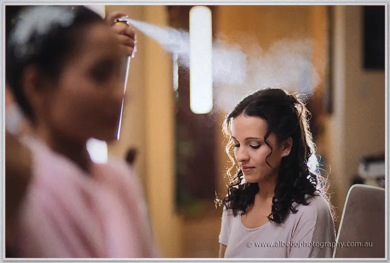 Hairspray mist catches the light over a bridesmaid with dark curls during morning preparations