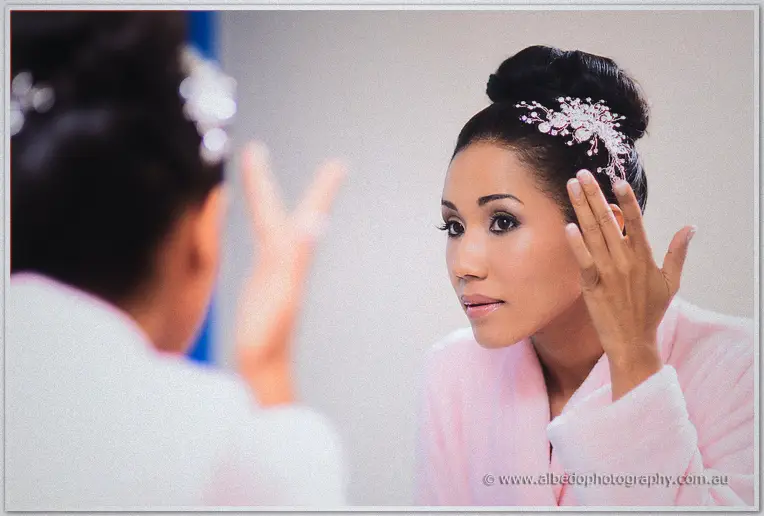 The bride touches her crystal hairpiece while checking her reflection in a bright mirror