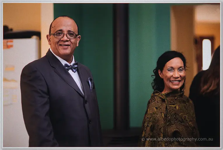 Troy's parents beam at the camera in the lounge, his father in a navy suit and bow tie