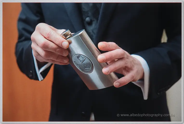 A groomsman's hands cradle an engraved stainless steel groomsmen flask against his navy suit