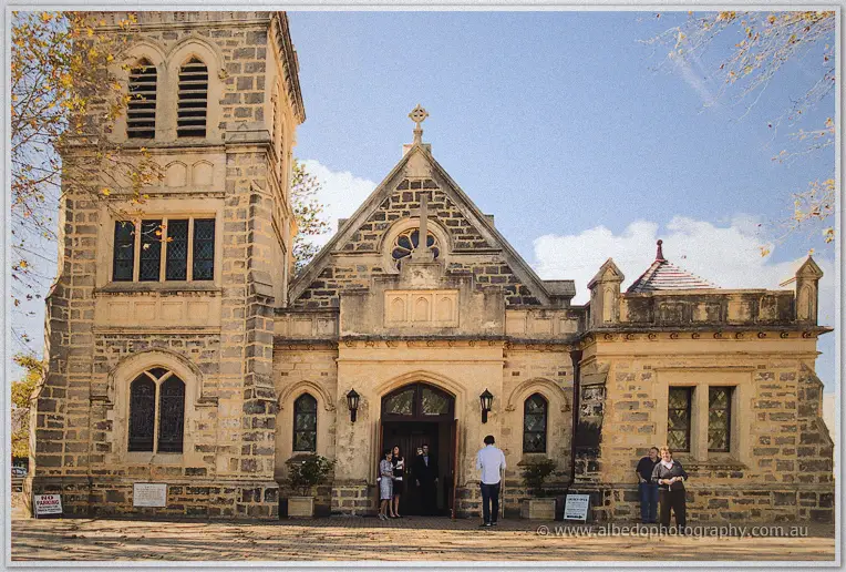 Guests gather at the arched doorway of the historic limestone church beneath a bright blue sky