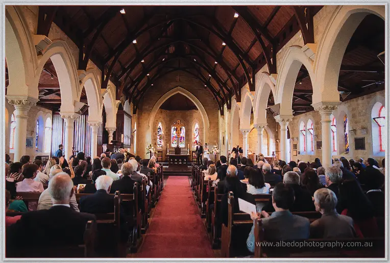 Guests pack the pews of the heritage church as the couple exchange vows beside the stained glass windows.