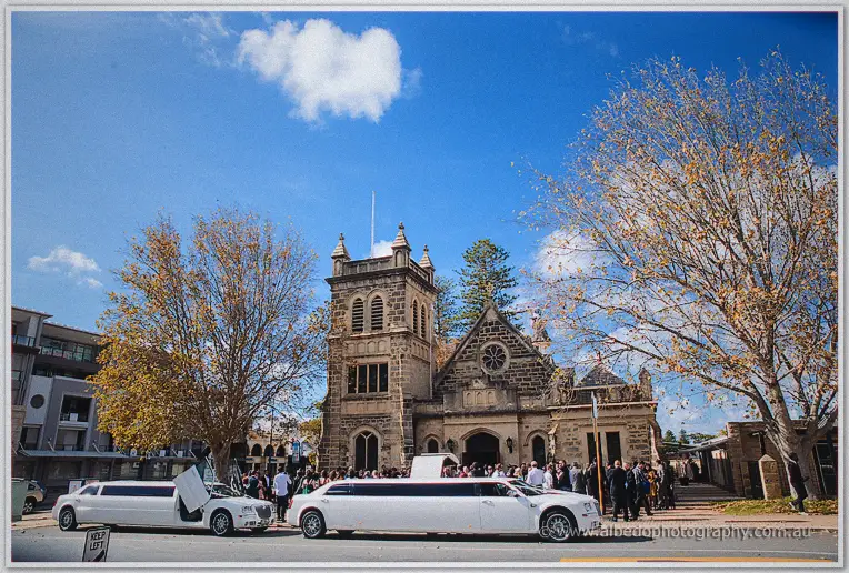 White stretch limousines wait under a blue sky outside the historic stone church tower in Christchurch.