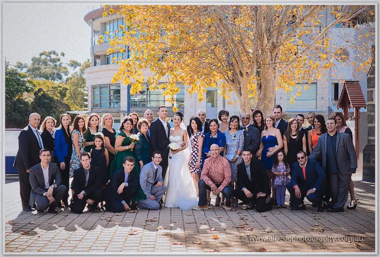Cristal and Troy stand front and centre of a big family group shot beneath autumn leaves and city buildings.
