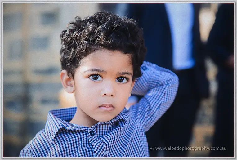 Close-up of a curly-haired boy in a checked shirt gazing at the camera during the outdoor family gathering.