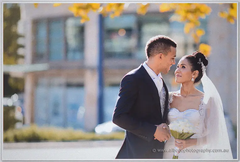 Cristal and Troy gaze at each other beneath golden foliage, city buildings blurred behind them.