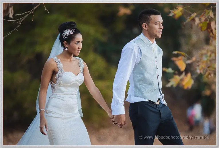 Cristal and Troy walk hand in hand through scattered autumn leaves, hedgerows soft behind them.