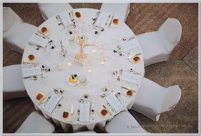 Overhead, a candlelit manzanita centrepiece anchors white menus and bread plates at each place setting.