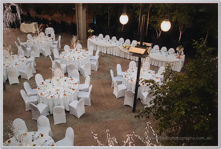Round tables in white covers and candlelit centrepieces fill the courtyard before guests arrive.