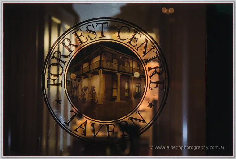 Etched glass reading Forrest Centre Tavern reflects the lamplit heritage verandah behind it.