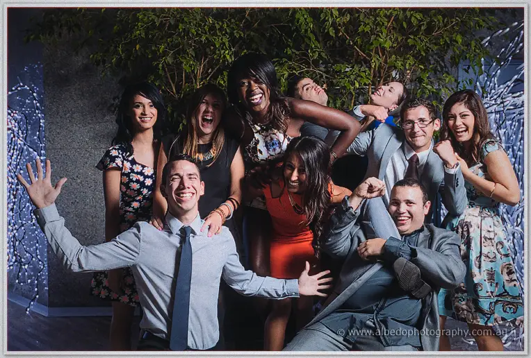 Young friends strike exaggerated poses for the camera against a fairy-lit wall.