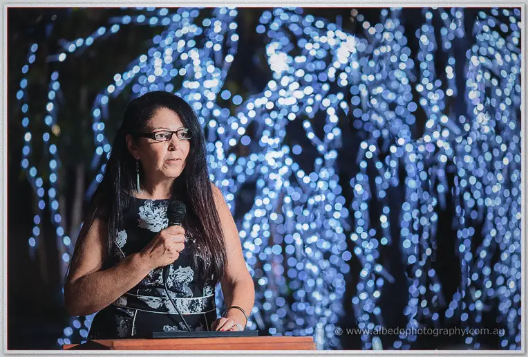 A guest in a floral dress delivers her speech beneath a canopy of blue fairy lights.
