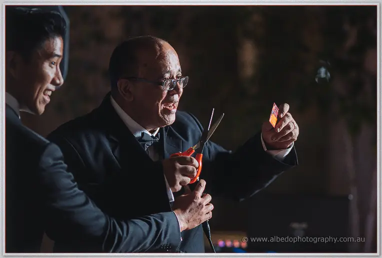 A man in black tie gestures mid-story while holding the microphone under glowing lights.
