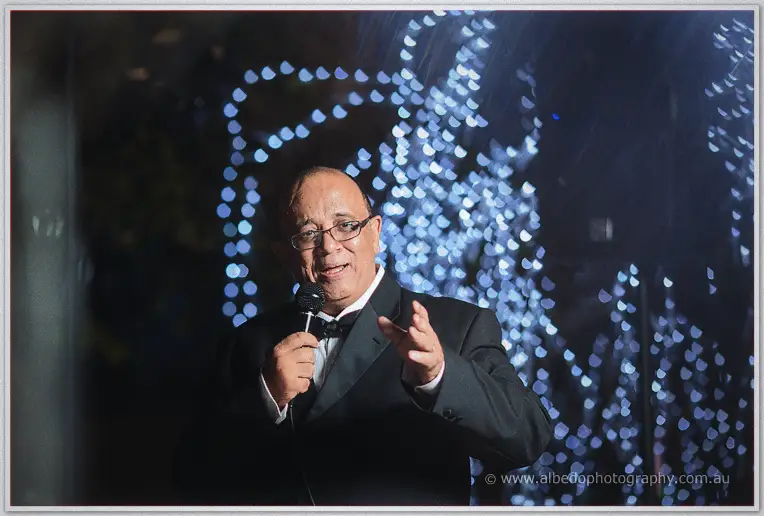 Wielding scissors and a small card, the speaker has the groom laughing along beside him.