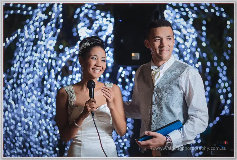 Microphone in hand, Cristal beams at the crowd while Troy waits beside her with her notes.