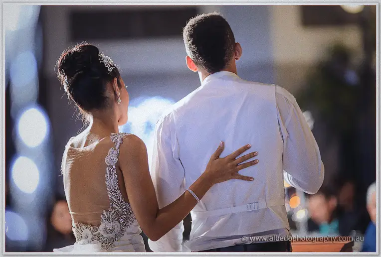 Cristal's hand presses against Troy's back as they turn to their guests, gown beaded and bare.