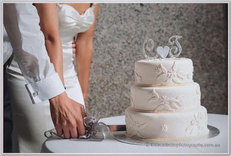 Close view of the couple's lace-patterned three-tier cake crowned with a sparkling C and T monogram topper
