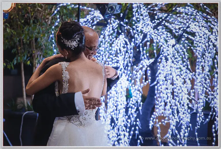 Cristal embraces her father beneath a willow tree wrapped in white fairy lights after the reception speeches