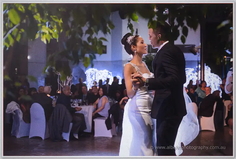 Cristal and Troy share their first dance beneath leafy trees while guests watch from candlelit tables
