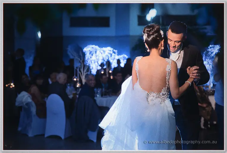 Troy grins over Cristal's sheer lace-backed gown during their first dance under blue-lit trees