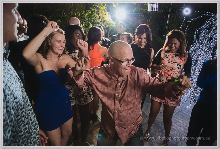 A bald guest in glasses dances wildly at the centre of a laughing crowd on the packed dance floor