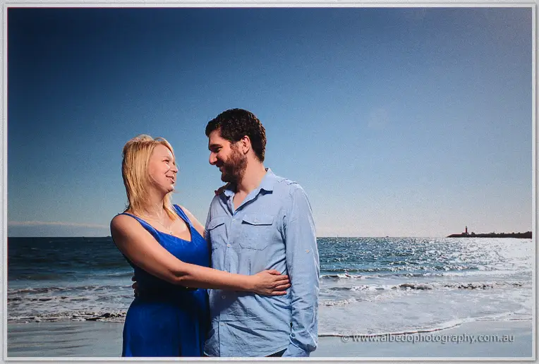 Julie hugs Dale close at the water's edge, both laughing as gentle waves roll in behind them
