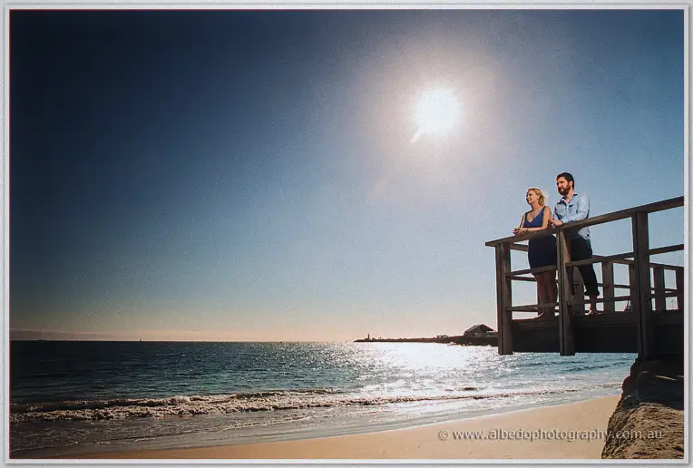Beneath a blazing sun, the couple lean on a timber jetty rail above the empty beach