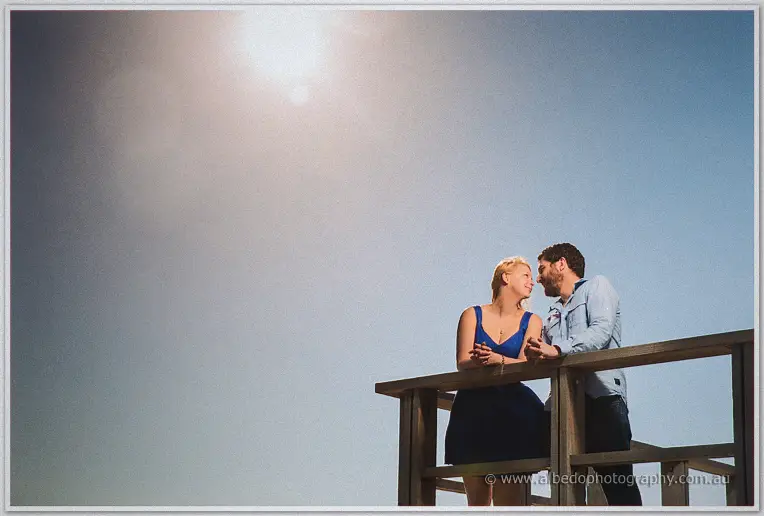 Dale and Julie lean into each other on a lookout rail, sunlight flaring across the pale sky