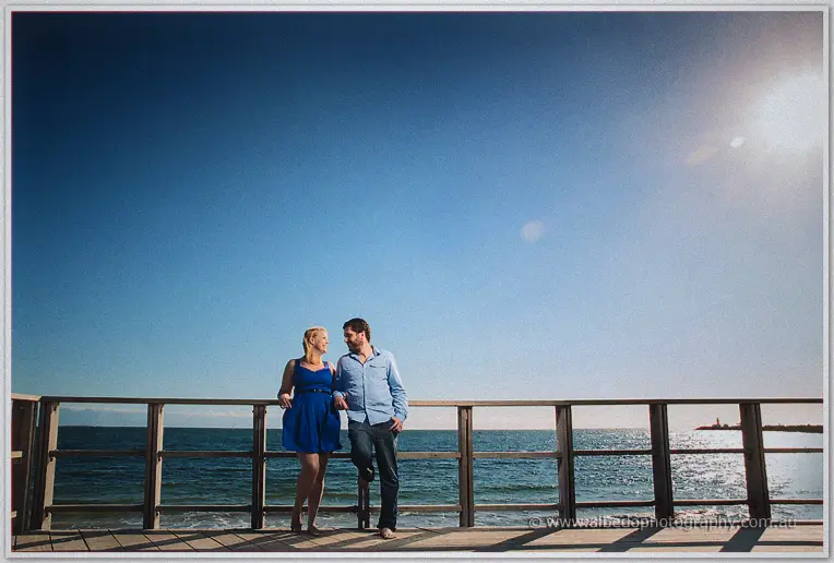 The couple share a laugh barefoot on the jetty, sea glittering through the haze behind