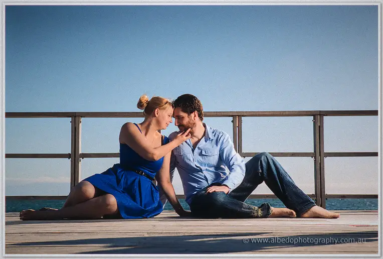 Sitting on the jetty boards, Julie playfully touches Dale's beard as they lean in close
