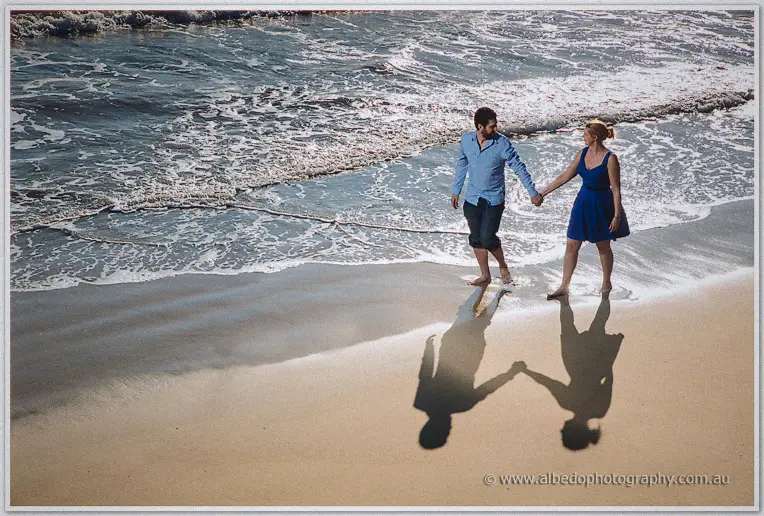 Wet footprints trail behind the couple as foamy surf chases them up the pale sand