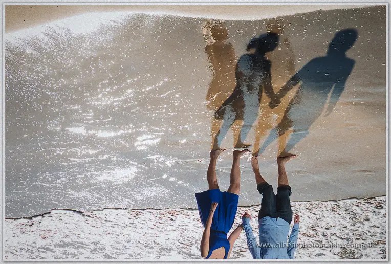 Long shadows stretch from Julie and Dale as they wander the mirror-wet sand at the waterline
