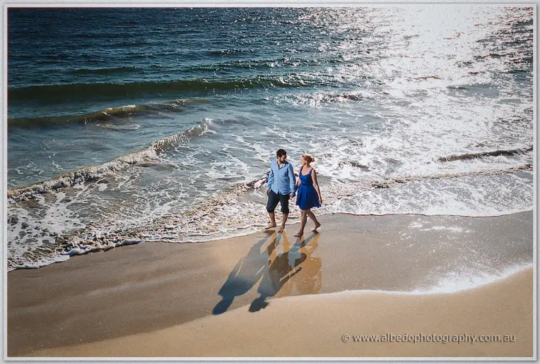 Looking straight down, Julie and Dale stand barefoot in the shallows, shadows meeting on the sand