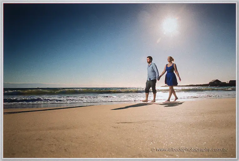 Hand in hand down the wide open beach, long shadows before them and sun high overhead
