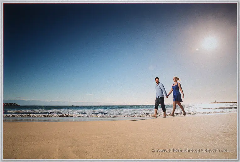 Barefoot in rolled trousers, Dale leads Julie along the waterline under a bright midday sun