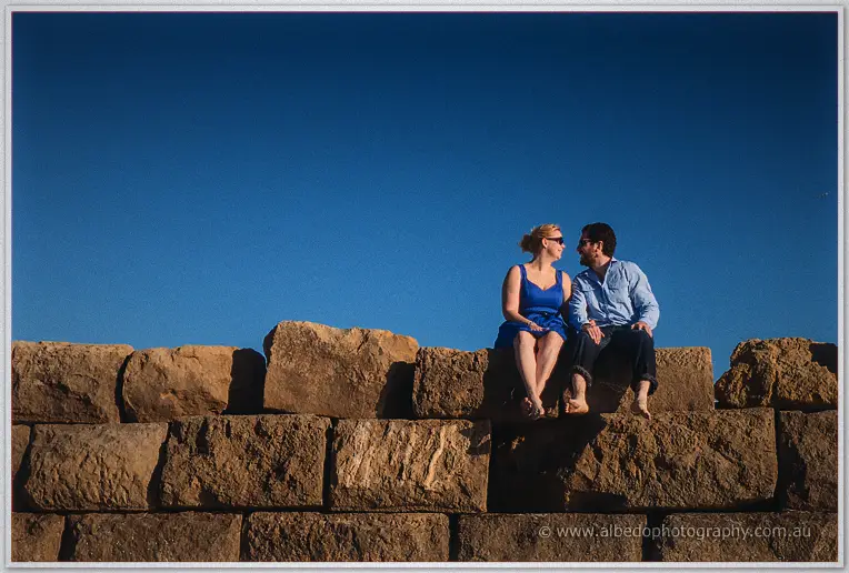 Perched on sun-warmed limestone blocks, Julie and Dale lean close under a deep blue sky