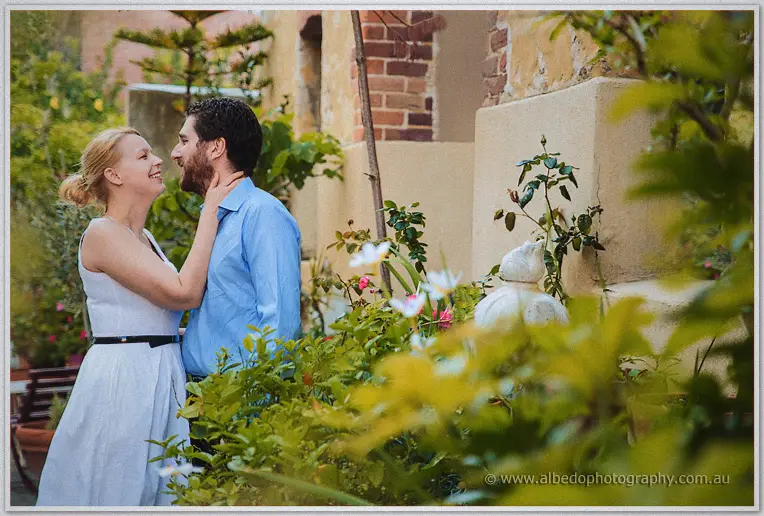 Amid roses in a cottage garden, Julie draws Dale near along a brick courtyard path