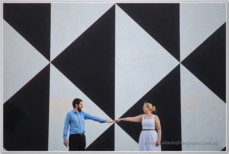 Dale and Julie reach across to touch fingertips beneath a towering geometric mural