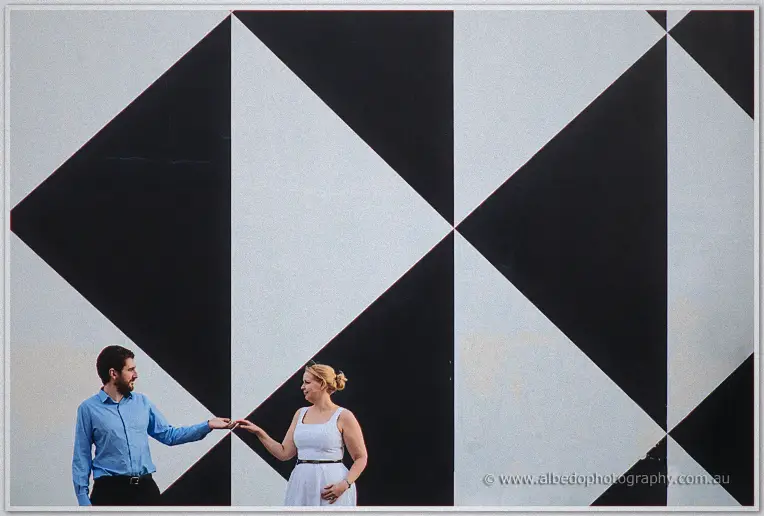 Side by side against the huge geometric mural, the couple lean in to clasp hands